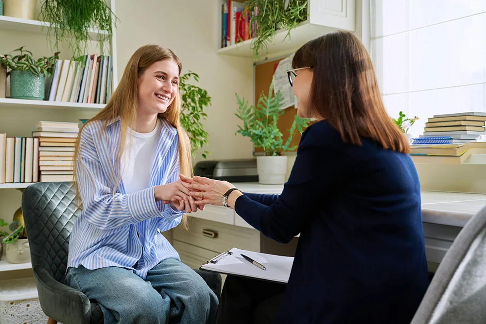 a teen holding hands with counselor in session