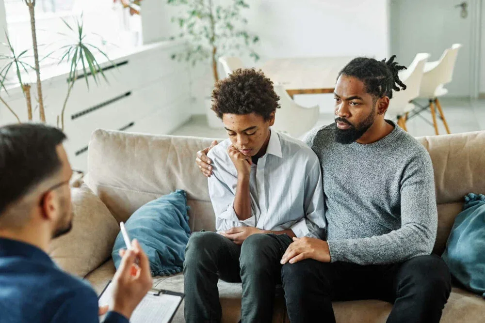 teen boy comforted by his dad during communication exercises in family therapy
